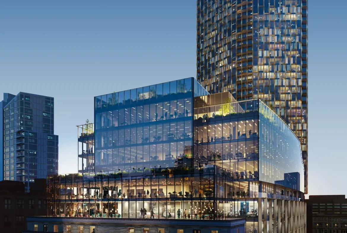 The glass exterior of No. 1 St Michael’s in Manchester, with illuminated offices and the tower rising behind